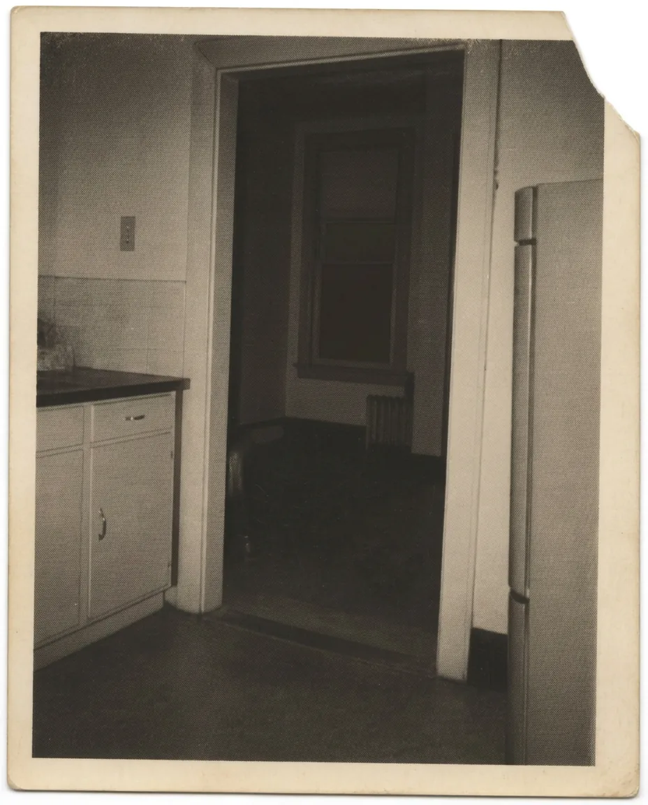 Small archival black and white photograph of a dim kitchen doorway at night